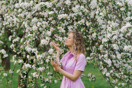 Thirty year old woman sniffs a branch of a flowering tree in the park in springの写真素材