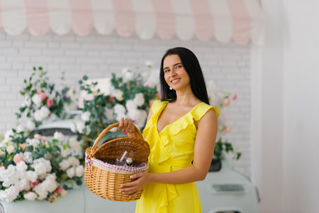 Cheerful young woman in a bright yellow dress holds a basket for a romantic picnicの写真素材