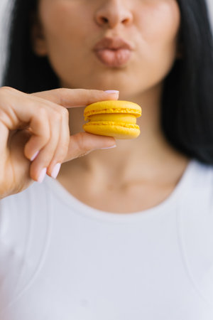 Close-up of yellow macaroons in the hands of a woman against the background of her mouth and lipsの写真素材