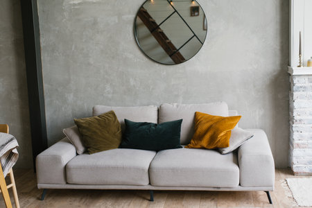 Gray sofa with pillows, round mirror hanging on the wall in a modern Scandinavian-style living roomの写真素材