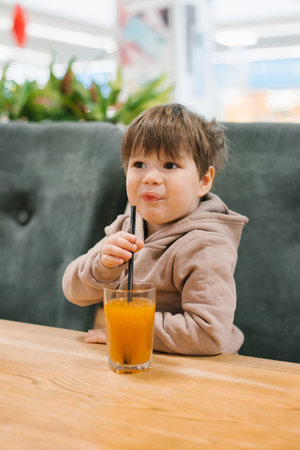 Little boy drinks juice from a straw while sitting at a table in a cafe. The child does not like a freshly squeezed drinkの写真素材