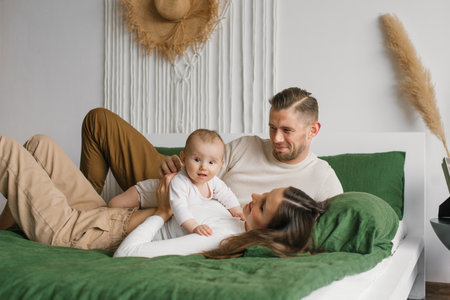Happy young family with a baby son rests and communicates with the child lying on the bed in the bedroomの写真素材