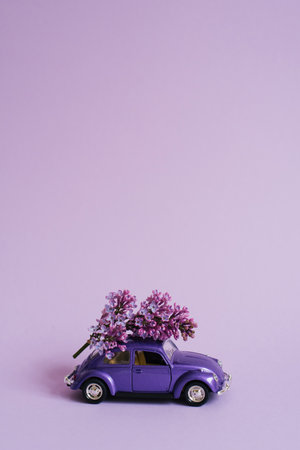 Purple toy car with lilac flowers on the roof on a lilac background. flower delivery. Birthday holiday concept, Mother's day, Valentine's day, Spring dayのeditorial素材