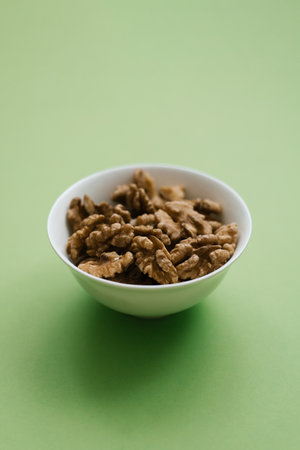 Peeled walnuts on a white plate on a green background with a copy space. Source of iron and mineralsの写真素材