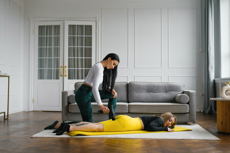 Female massage therapist does massage exercises on the hips with the help of a shock vibrator...