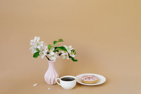 Beautiful white apple tree flowers in a white vase, donuts and a cup of tea on a beige background with a copy spaceの写真素材