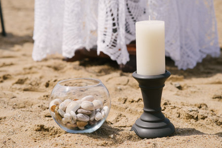 Decor of a romantic dinner by the sea or ocean. A candle on a candlestick and sea stones in a glass vaseの写真素材