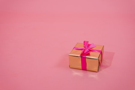 Gift box in gold paper decorated with fuchsia bow on pink background with copy spaceの写真素材