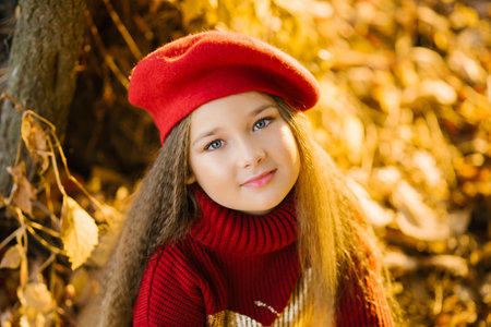 Beautiful girl in a red beret is sitting near a tree in autumnの写真素材