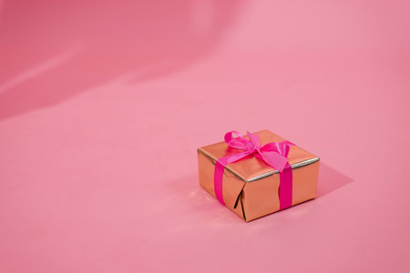 Gift box on pink background. A gift in gold paper, decorated with a stylish elegant fuchsia satin ribbon bow. The concept of Christmas and any other holidaysの写真素材