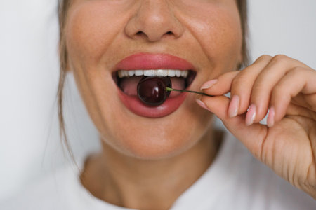 Woman with beautiful white teeth happily eats cherry close-upの写真素材