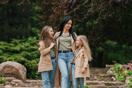 Stylish Caucasian mom and her two daughters are chatting and walking in a spring blooming park. Mother's Day and a happy familyの写真素材