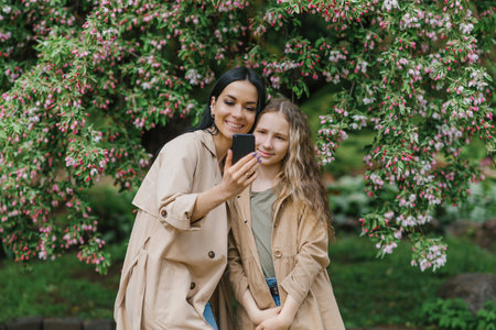 Happy family mom and her adorable teen daughter in the spring in the park selfie with a smartphoneの写真素材