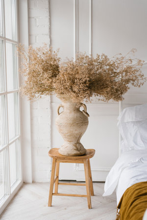 Dried flowers in a classic vase on the bedside table with pillows near the French windowの写真素材