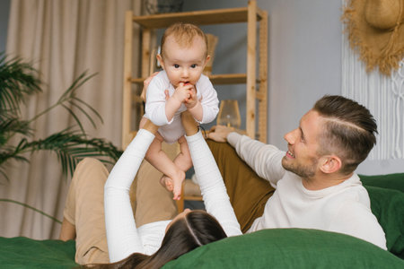 Happy family with smiles and a baby are lying and resting on the bed in their house