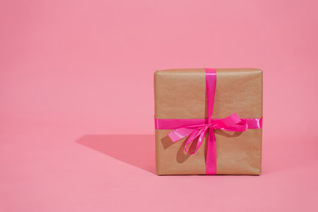 Gift box on pink background. A gift in gold paper, decorated with a stylish elegant fuchsia satin ribbon bow. The concept of Christmas and any other holidaysの写真素材
