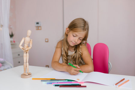 Seven year old schoolgirl is doing homework at her desk at home or at school, drawing with felt-tip...