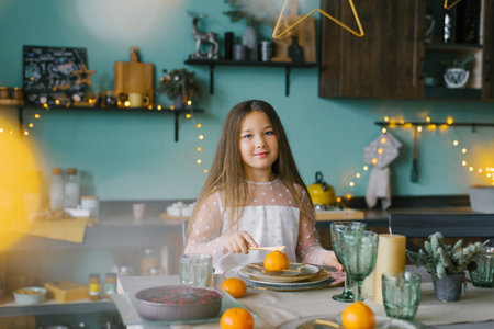 Cute baby girl is sitting at a festive table set for Christmas and eatingの写真素材