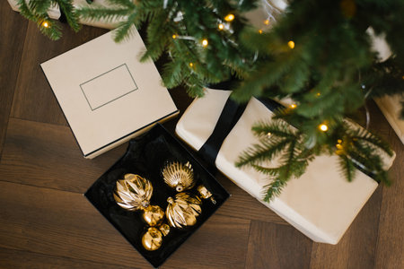Christmas box is a stylish gift with a black bow on it and golden toys under the Christmas tree for...