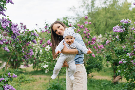 Happy European mother lifts up her little smiling son in her arms in the spring on a walk in the parkの写真素材
