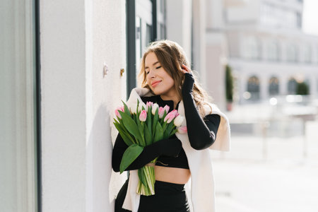 Young woman is distracted from her daily routine, enjoying the beauty of tulips, walking around the cityの写真素材