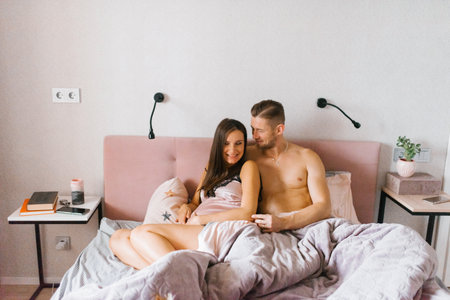 Husband and wife sit on the bed on a day off in the morning and communicate with conversation and smilesの写真素材