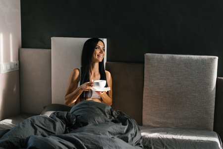 Young caucasian women resting after sleep in cozy bed in hotel, and drinking morning coffee or teaの写真素材