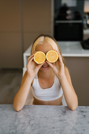 Child holding orange slice in front of her eyes at the kitchen tableの写真素材