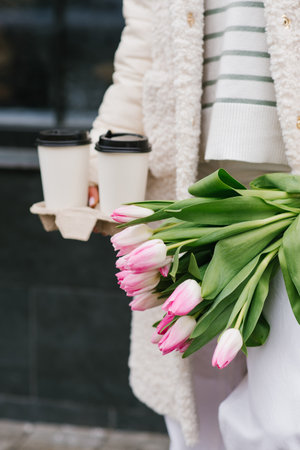 Bouquet of pink tulips and takeaway coffee in the hands of a young stylish womanの写真素材
