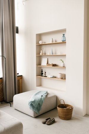 Modern living room with pouf with blue blanket. Built-in shelves in the wall with decor, personal accessories, ceramics in Scandinavian minimalist styleの写真素材