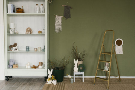 Green room with a white bookshelf and a staircase, decorated for Easter. There are many items on the bookshelf, including a horse figurine and several books. The ladder is leaning against the wallの写真素材