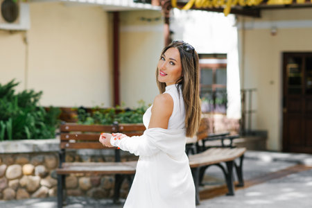 Happy young woman in white casual clothes smiles while walking through the city streets in summerの写真素材