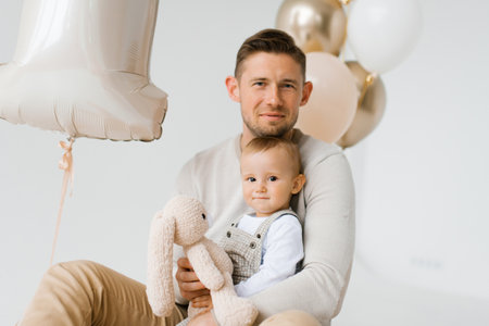 Happy family dad and one year old son sitting in the background of birthday balloonsの写真素材