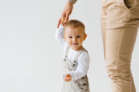 Father holds the hand of a one-year-old boy's child son. The child is wearing a white shirt and overallsの写真素材