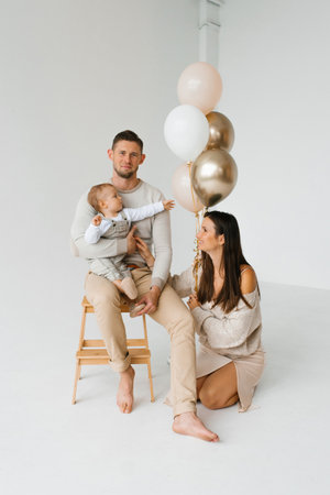 Happy young family of dad, mom and one-year-old son celebrate his birthday with balloonsの写真素材