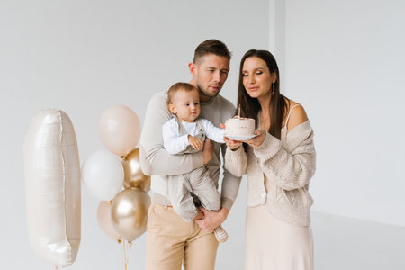 Young family with a one-year-old son blows out a candle on a birthday cake. The scene is joyful and festiveの写真素材