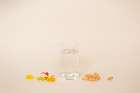 Glass of water is next to a pile of pills and candy. Concept of a healthy lifestyle, with the water representing hydration and the pills and candy representing the need for balanceの写真素材