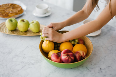 Close up of children's hands of a girl taking fresh fruit from a plate on the table in the kitchenの写真素材