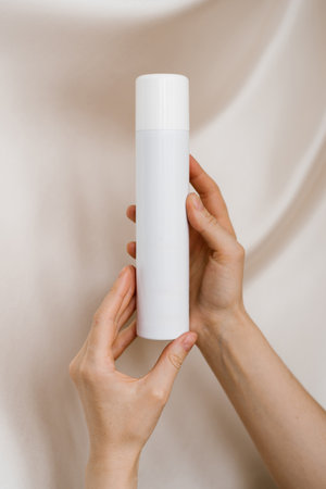 Woman's hands holds a bottle in her hands against a background of soft organza fabricの写真素材