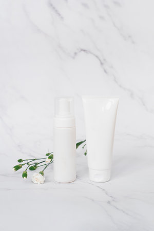 Two white bottles of lotion cosmetic and a small container of cream sit on a marble countertop. The lotion and cream are both white and have a clear plastic topの写真素材