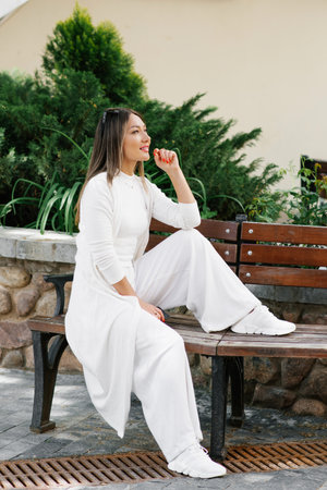 Caucasian woman in a white dress and white pants sits on a bench in a cityの写真素材
