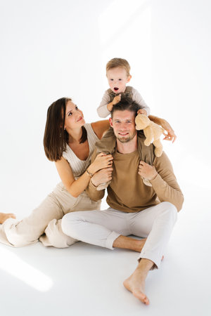 Mother and father hold their two year old son and a teddy bear in their armsの写真素材