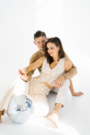 Young man and woman are sitting together on a white surface. They are both smiling and seem to be...