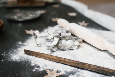 Wooden board with a pile of cookie cutters and a rolling pin on it. The scene suggests that someone...