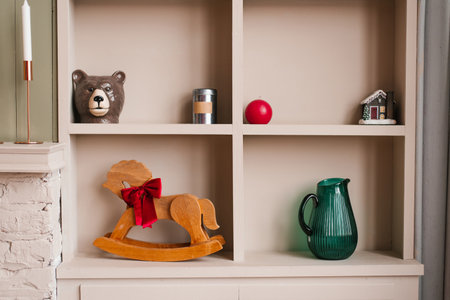 Wooden rocking horse on a shelf next to a green pitcher and a red candle. Cozy and inviting living roomの写真素材