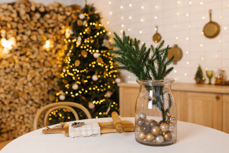 Branch of fir tree in glass vase stands on table against the background of Christmas tree in the dining roomの写真素材