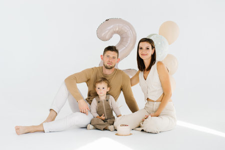 Happy family of three, father, mother and child, are going for a picture with balloons and birthday cakeの写真素材