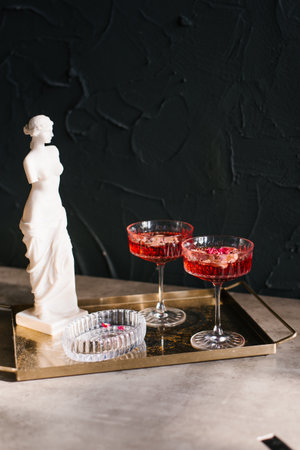 White statue of woman stands next to two glasses of red wine on tray on table. Concept of sophistication and eleganceの写真素材