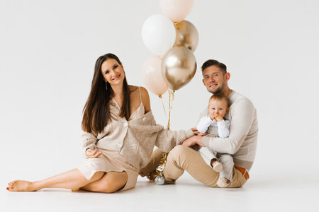 Happy family with a one year old birthday boy are sitting on the floor next to balloonsの写真素材