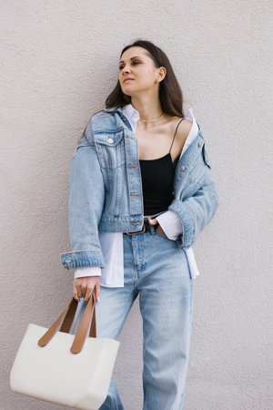 Young caucasian woman in a blue jacket and jeans is holding a white purseの写真素材